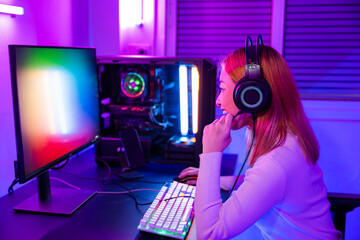 Wall Mural - Happy Gamer endeavor plays online video games tournament with computer neon lights, young woman wearing gaming headphones intend to do playing live stream games online at home