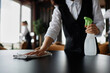 © Seventyfour - Close up of server wiping dining table in restaurant preparing for opening, copy space