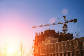 construction crane is building a residential building on a construction site against background of blue sky with the sun