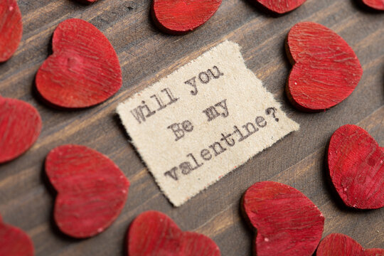 Will you be my Valentine - typed text. Valentines Day greetings concept. Little red wooden hearts close up. Valentines greeting card.
