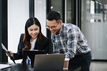 Business, technology and office concept - two businessmen with laptop, tablet pc computer and papers having discussion in modern office.