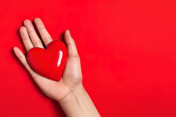 hand holds a red heart love shape on a red background with copy space