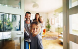 Fototapeta  - A friendly family welcomes guests at the door of their new home. A young boy holds the door open and smiles at the camera. Behind him we see his smiling family and the bright interior. Generative ai