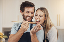 Couple, cooking and taste test in kitchen with romance, support and love in their home together. Food, spoon and man feeding woman in house while preparing a delicious meal with fun and bonding