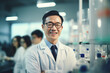 © ND STOCK - A beautiful Asian male scientist stands in a white coat and glasses in a modern medical science laboratory with a team of experts in the background.