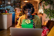 © Marko Geber - Happy young African American woman showing her gifts on a video call from her home decorated for the Christmas holidays