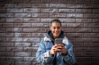 © Marko Geber - Portrait of a young smiling woman using a smartphone with a brick wall background