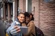 © Marko Geber - Young mixed lesbian couple taking a selfie on the smartphone while having a stroll together in the city