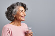 © SOLDATOOFF - Portrait of a smiling fifty year old Latina woman with smoothie glass in hand on gray background with copy space.