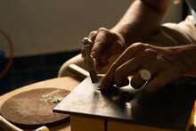 Goldsmith's Hands Hammering Jewelry Stone On A Wooden Plate In A Goldsmith's Workshop. Natural Light And Warm Atmosphere