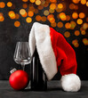 Christmas card bottle with wine, glass, santa hat on a dark background