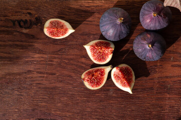 Wall Mural - Whole and cut fig fruits on brown wooden board, flat lay. Healthy nutrition, autumn fruit diet concept, fiber source