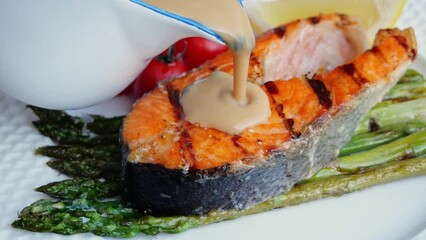 Sticker - Grilled salmon steak pouring cream brown sauce. Slow Motion. Close up. Baked salmon fillets on a grill plate asparagus and tomatoes