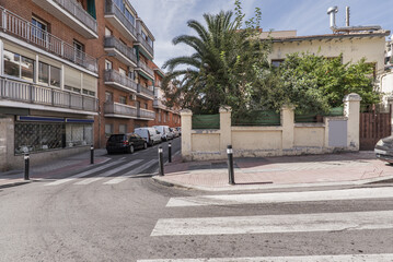 A street intersection with zebra crossings next to a single-family home with a palm tree in the garden