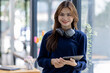© David - Young adult happy smiling Hispanic Asian student wearing headphones standing indoor using digital tablet in university campus or at virtual office. College female student learning remotely.