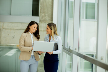 Two young business women with laptop in the office hallway