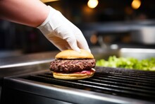 Hand Flipping A Burger Patty On A Hot Griddle