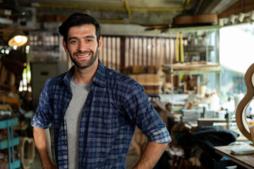 Wall Mural - Portrait of a young handsome carpenter wearing a plaid shirt and apron, smiling in his workshop.