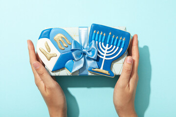 Wall Mural - Gingerbread on gift box in female hands on blue background, top view