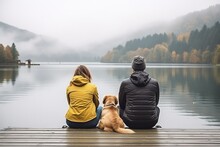 A Family With A Small Yellow Dog Is Resting On The Pier And Looking At The Lake