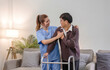 © wichayada - young asian female nurse care giver helping asian senior old man with mobility walker in living area of nursing home senior daycare center. Nurse take care elderly patient with cheerful concentrate