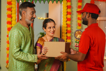 Senior couples receiving parcel or package from delivery person at home door during Diwali festival day - concept of online order, quick commerce and festive gift or present.