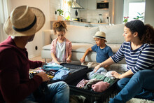 Young Mixed Family Packing Their Clothes In A Suitcase For Their Trip In The Living Room At Home