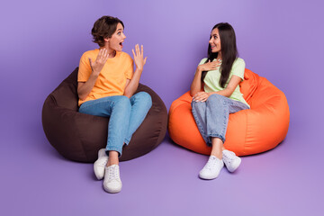 Wall Mural - Photo of positive impressed ladies wear t-shirts sitting bean bags discussing last news isolated violet color background