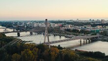 Aerial View Suspension Bridge In Modern City Backlit With Orange Sunlight. Drone Flying Above Bridge Overlooking Downtown Skyscrapers Urban Skyline, Evening Sunset Light, High Rise Buildings Horizon
