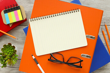 Wall Mural - Blank notepad and pen on an orange folder with glasses on a wooden table. Top view with copy space in bright light colors, flat lay.