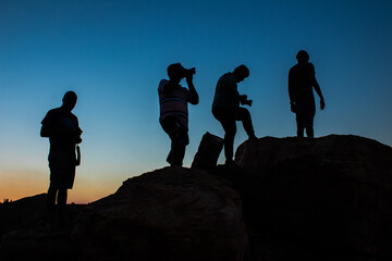 silhouette of Group of male photographers standing or taking photograph on top the mountain in evening sunset with blue sky on the background