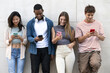 © carlesiturbe - Diverse group of young people texting leaning against a wall. Happy group of friends using their phones in the street.