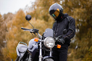 motorcyclist in motorcycle gear and helmet near a classic motorcycle in autumn