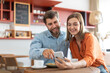 © Home-stock - Happy european couple using smartphone, sitting in cafe together on daytime, surfing internet or shopping online. Modern relationships concept