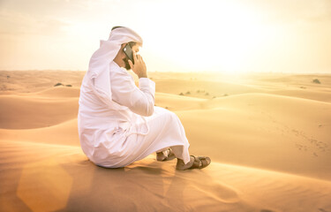 Wall Mural - Arabic man with traditional emirates clothes walking in the desert