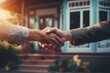 A handshake shared by two individuals as they complete the sale of a house, with the house in view