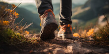 Man Hiking Up A Mountain Trail With A Close-up Of His Leather Hiking Boots. The Hiker Shown In Motion, With One Foot Lifted Off The Ground And The Other Planted On The Mountain Trail. 