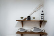 decorative fish, lighthouse and plants against white wall on wooden shelves form nautical seaside display