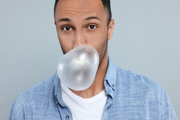 Wall Mural - Portrait of young man blowing bubble gum on light grey background