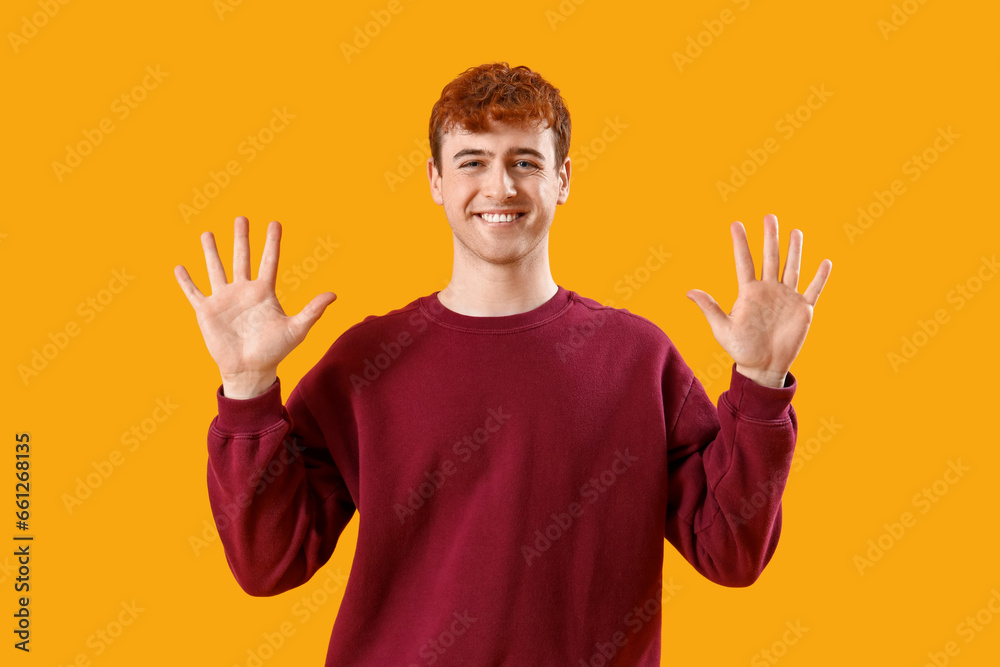 Young redhead man showing hands on yellow background