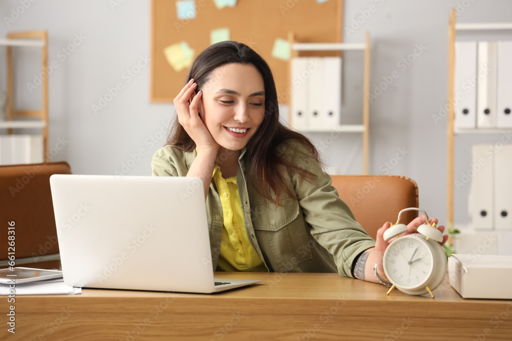 Young businesswoman with alarm clock in office