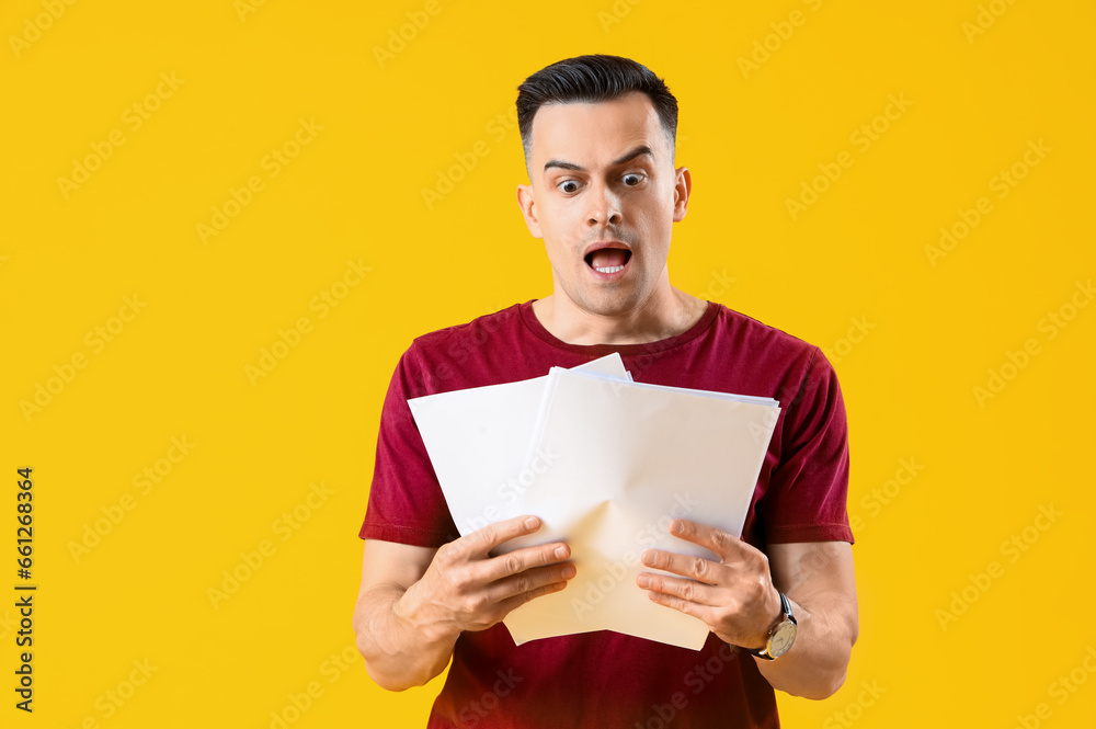 Stressed young man with documents on yellow background. Deadline concept