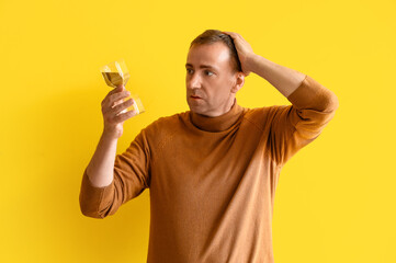 Wall Mural - Stressed mature man with hourglass on yellow background. Deadline concept