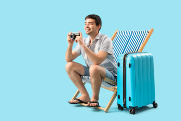 Sticker - Young man with photo camera and suitcase sitting in deck chair on blue background