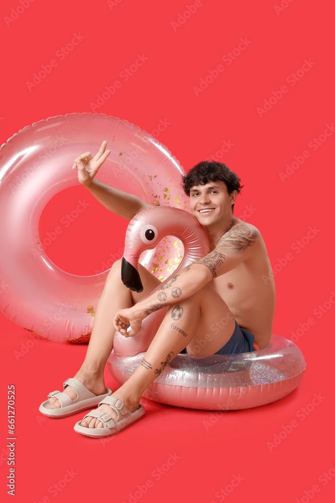 Young man with swim rings showing victory gesture on red background