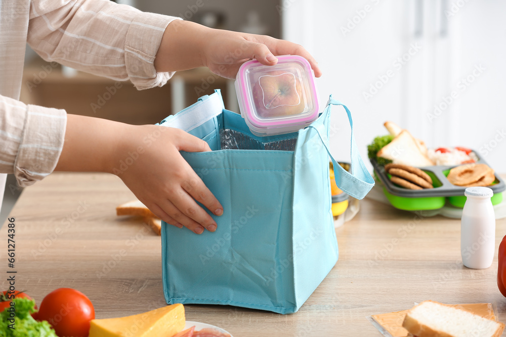 Mother packing meal for school lunch on table in kitchen