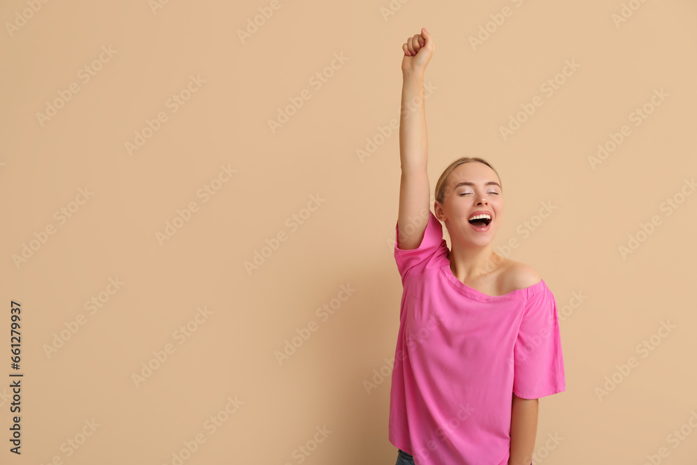 Happy young woman celebrating success on beige background