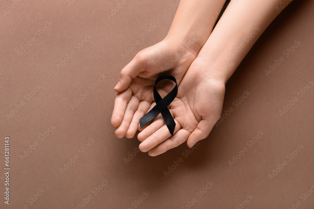 Woman holding black funeral ribbon on brown background