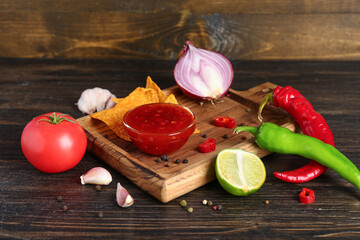 Wooden board with tasty salsa sauce, nachos and ingredients on wooden background