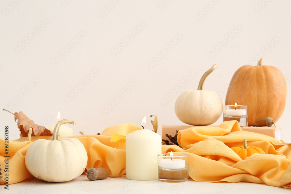 Burning candles with scarf, pumpkins and acorns on white background